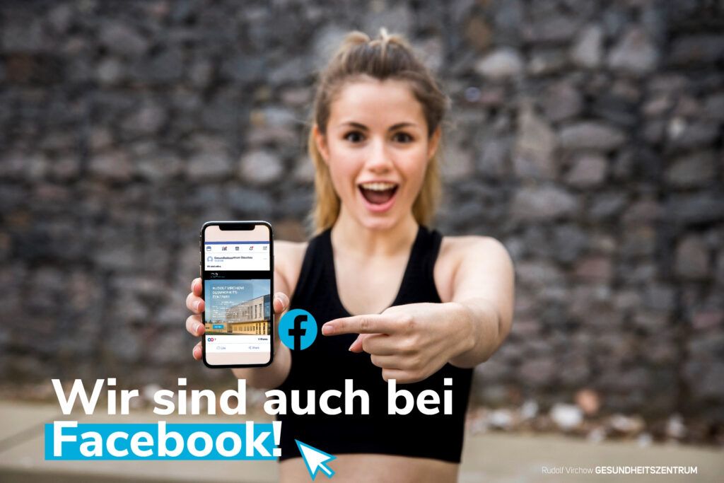 Frau zeigt auf Handy mit Facebookseite des Gesundheitszentrum