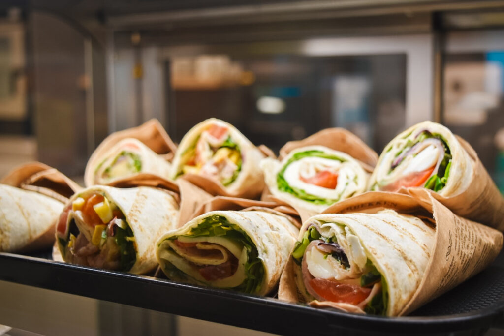 Verschiedene frisch zubereitete Wraps mit Salat, Gemüse und Käse, appetitlich angerichtet in einer Vitrine.