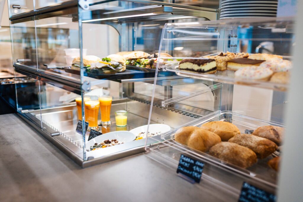 Eine gut gefüllte Verkaufsvitrine mit verschiedenen Backwaren, belegten Brötchen, Kuchenstücken, Säften und Müsli.