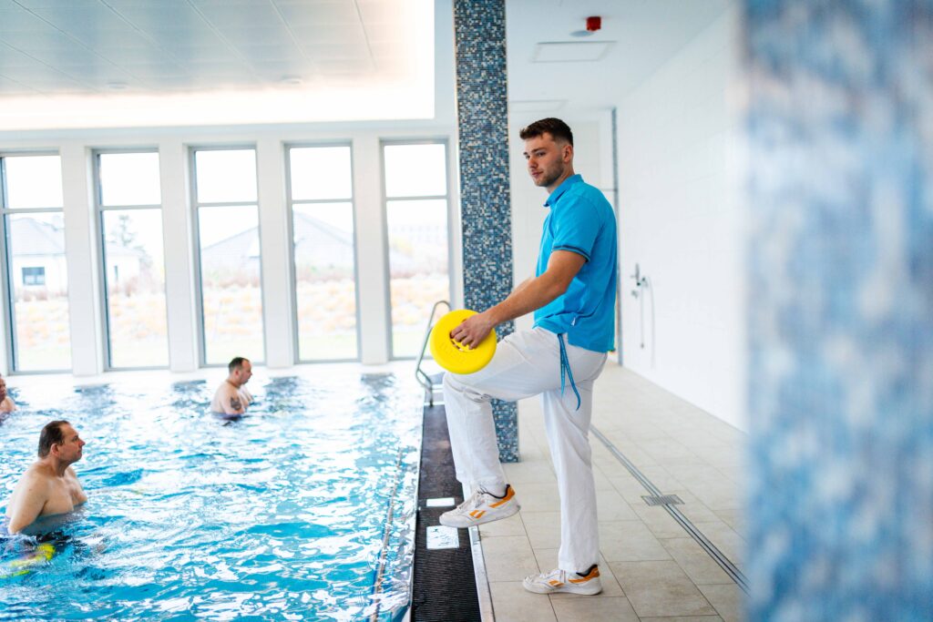Physiotherapeut leitet Wassergymnastik am Beckenrand des Therapiebeckens an