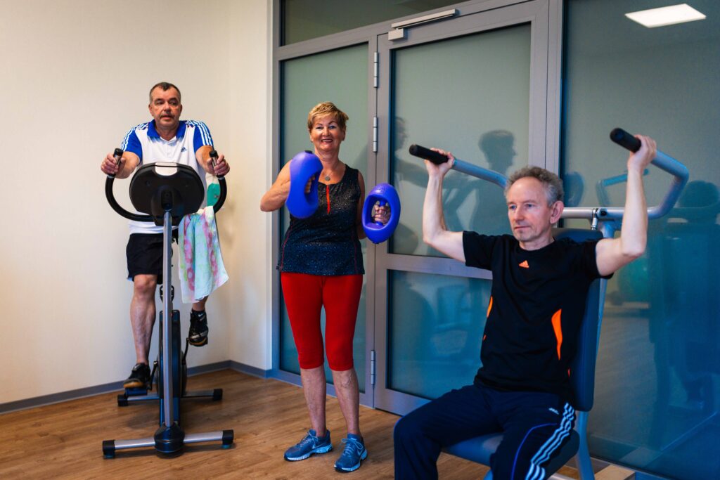 Drei ältere Menschen beim Training an Fitnessgeräten in einer Physiotherapie-Praxis