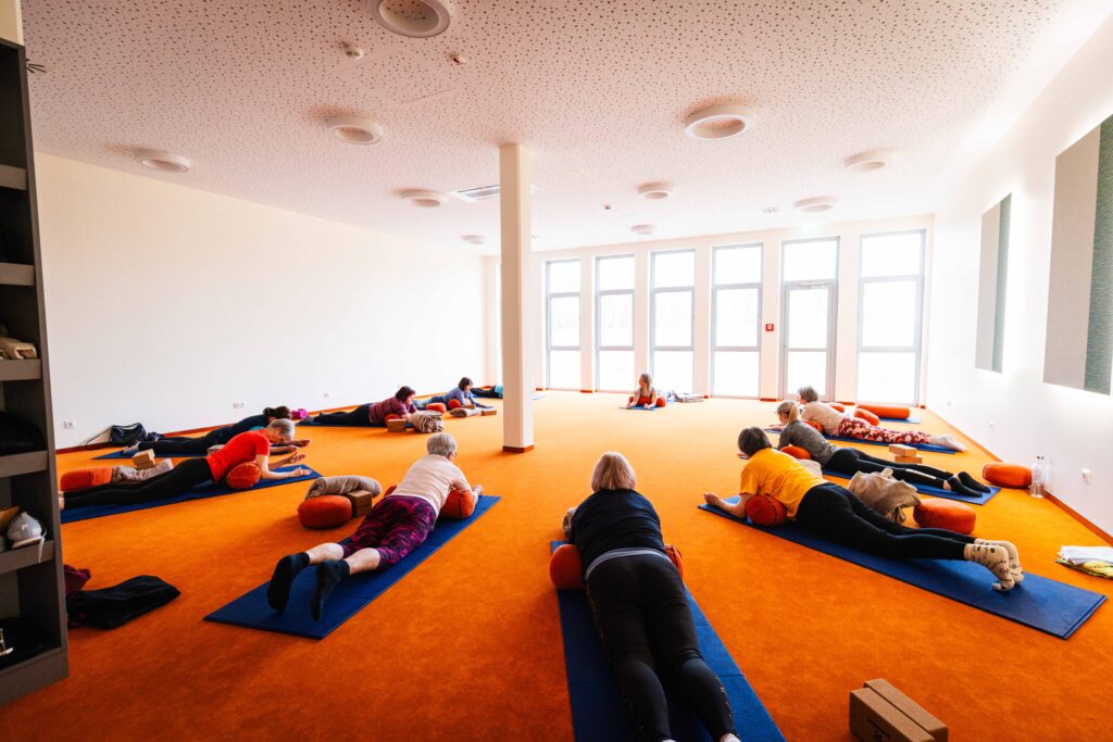Yogagruppe liegt auf Matten im lichtdurchfluteten Kursraum während einer Entspannungsübung